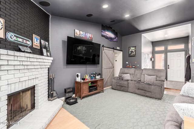 living room with a brick fireplace, a barn door, vaulted ceiling, and wood finished floors