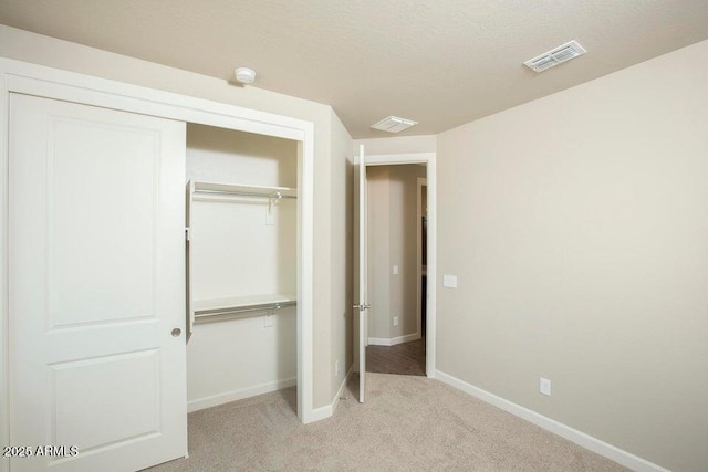 unfurnished bedroom featuring a textured ceiling, a closet, and light colored carpet