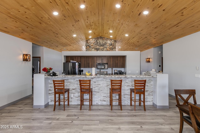 kitchen with lofted ceiling, wood ceiling, light hardwood / wood-style flooring, stainless steel refrigerator, and light stone countertops