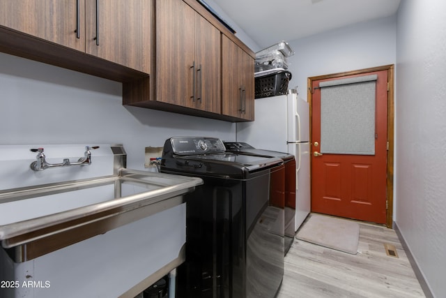 laundry room with sink, washer and clothes dryer, cabinets, and light wood-type flooring