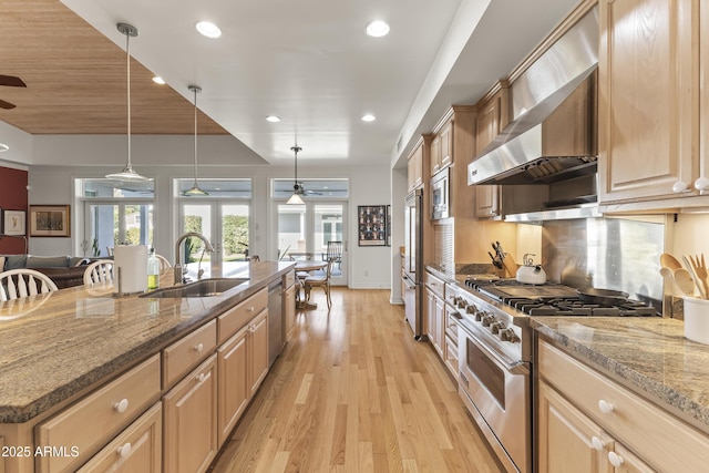 kitchen featuring stone counters, sink, wall chimney exhaust hood, pendant lighting, and appliances with stainless steel finishes