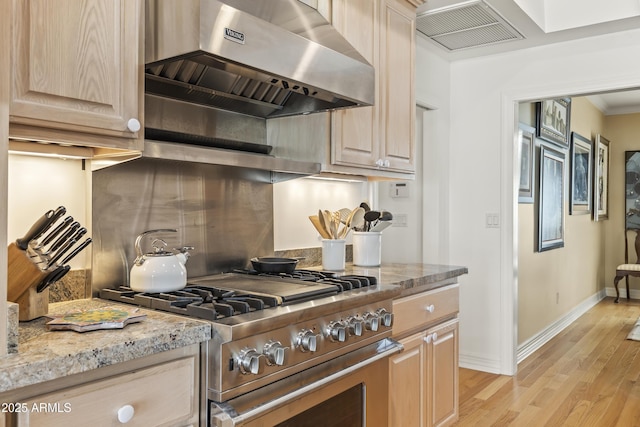 kitchen featuring light stone countertops, light brown cabinets, exhaust hood, and stainless steel range oven