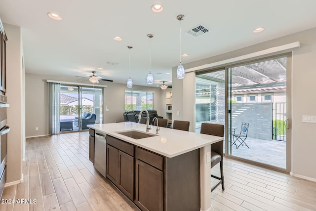 kitchen with a kitchen island with sink, pendant lighting, light hardwood / wood-style flooring, sink, and stainless steel dishwasher