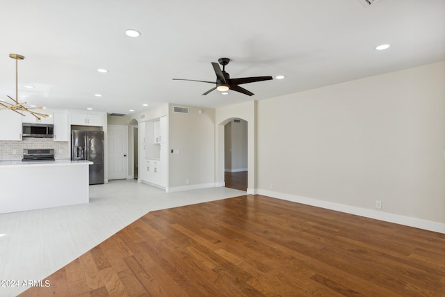 unfurnished living room featuring light wood-type flooring, baseboards, recessed lighting, arched walkways, and ceiling fan with notable chandelier