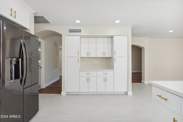 kitchen featuring light countertops, backsplash, stainless steel refrigerator with ice dispenser, visible vents, and arched walkways