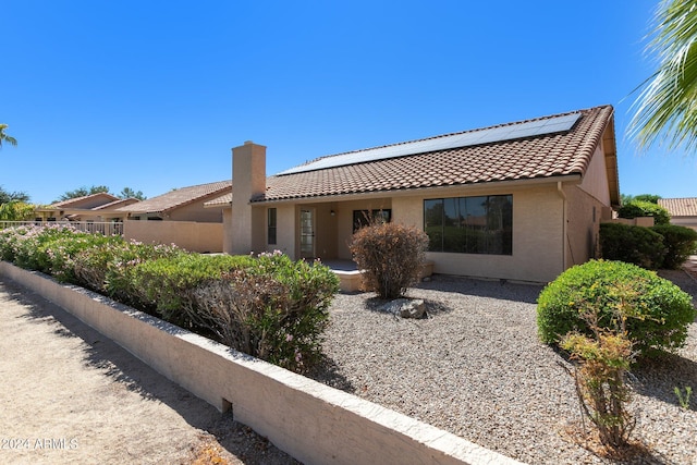 view of front facade with solar panels, a tiled roof, fence, and stucco siding