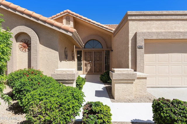 view of exterior entry with a tiled roof, a garage, and stucco siding