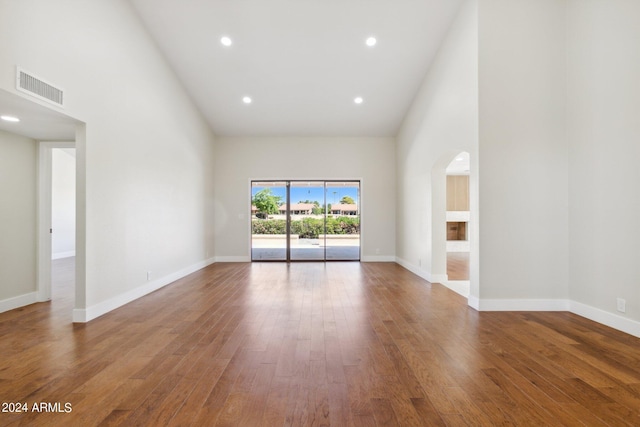 spare room with high vaulted ceiling, arched walkways, visible vents, and wood finished floors