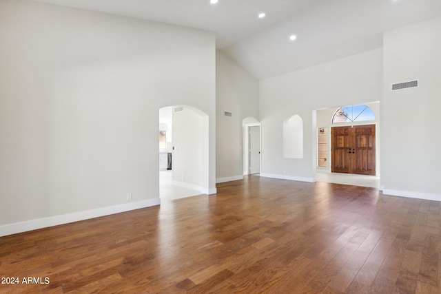 unfurnished living room with visible vents, baseboards, arched walkways, wood finished floors, and high vaulted ceiling