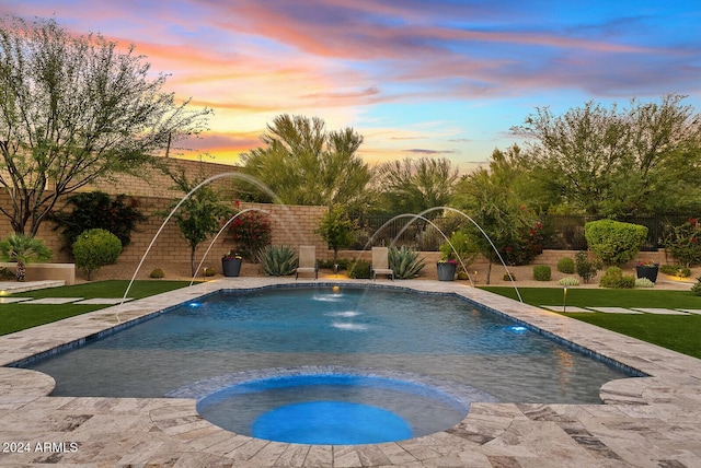 pool at dusk with an in ground hot tub, pool water feature, and a lawn