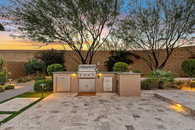 patio terrace at dusk with an outdoor kitchen, area for grilling, and sink