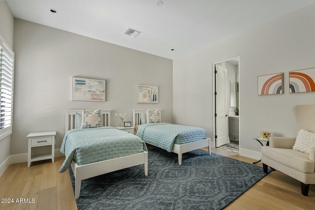 bedroom with connected bathroom, light hardwood / wood-style flooring, and multiple windows