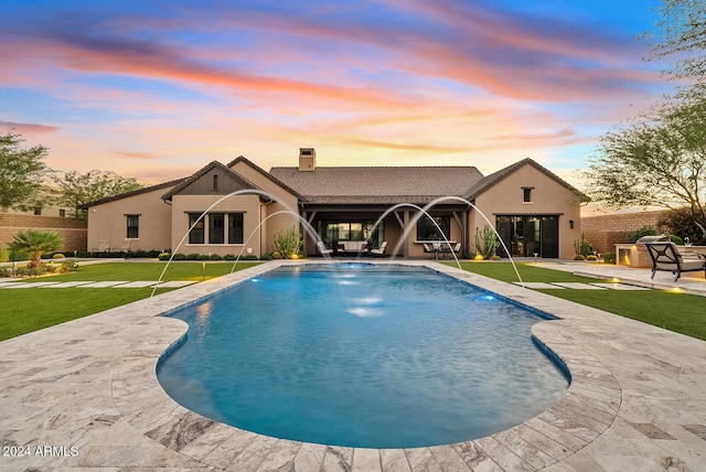 pool at dusk with a yard, pool water feature, and a patio area