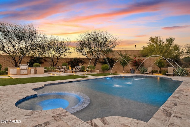 pool at dusk with an in ground hot tub, area for grilling, pool water feature, exterior kitchen, and a patio