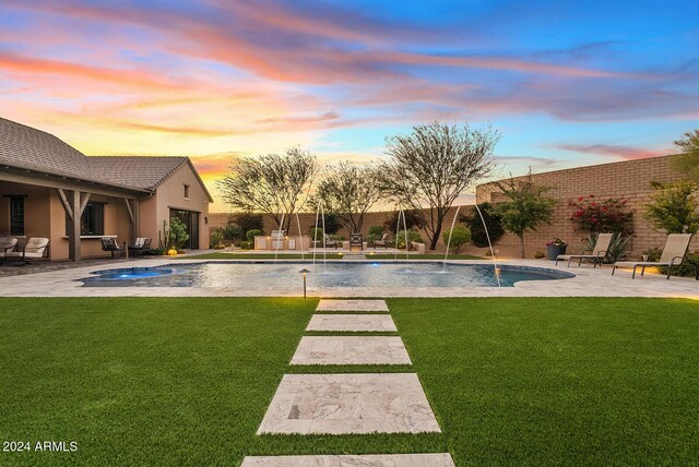 pool at dusk with pool water feature, a patio area, a yard, and an in ground hot tub