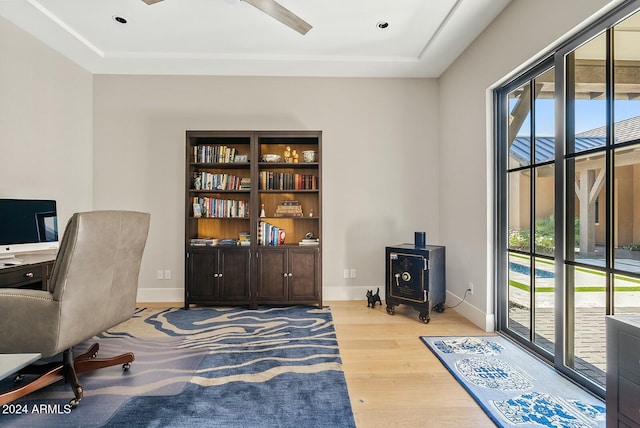 office area featuring a raised ceiling, light hardwood / wood-style flooring, ceiling fan, and a healthy amount of sunlight