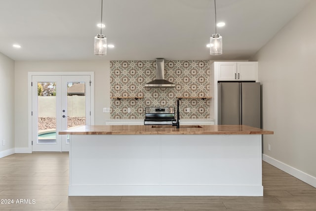 kitchen with stove, hardwood / wood-style floors, an island with sink, wall chimney exhaust hood, and stainless steel refrigerator