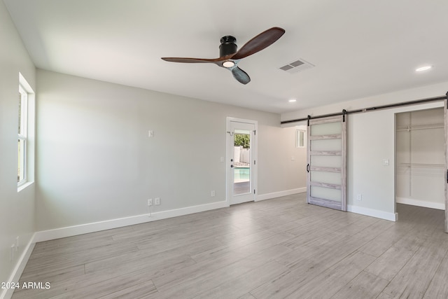 unfurnished bedroom featuring a walk in closet, light wood-type flooring, access to outside, ceiling fan, and a barn door