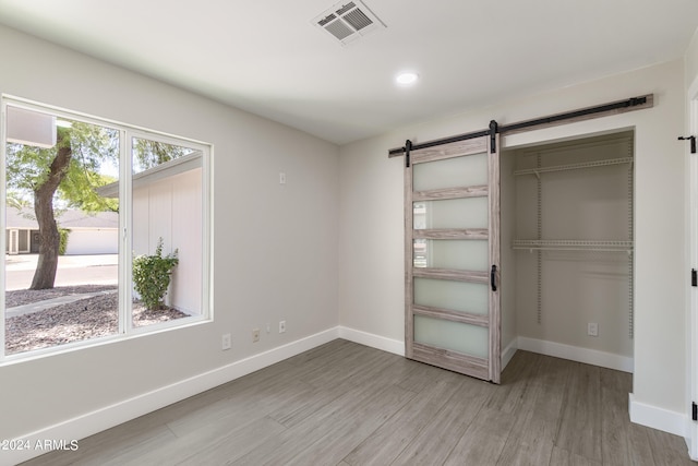 unfurnished bedroom featuring ceiling fan, a barn door, light hardwood / wood-style floors, and a closet