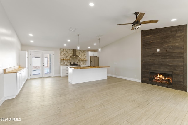 unfurnished living room with a fireplace, lofted ceiling, light hardwood / wood-style flooring, ceiling fan, and french doors