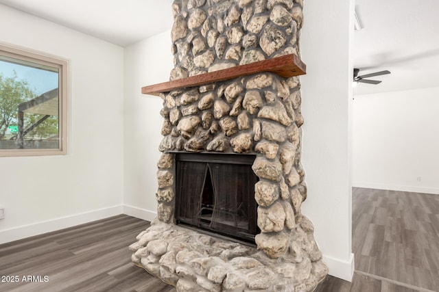 room details with baseboards, a stone fireplace, and wood finished floors