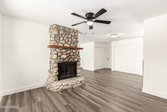 unfurnished living room featuring baseboards, ceiling fan, a stone fireplace, and wood finished floors