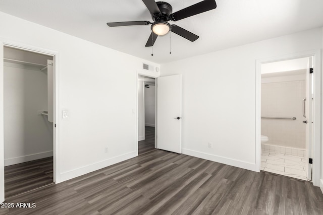 unfurnished bedroom with baseboards, a walk in closet, wood finished floors, and visible vents