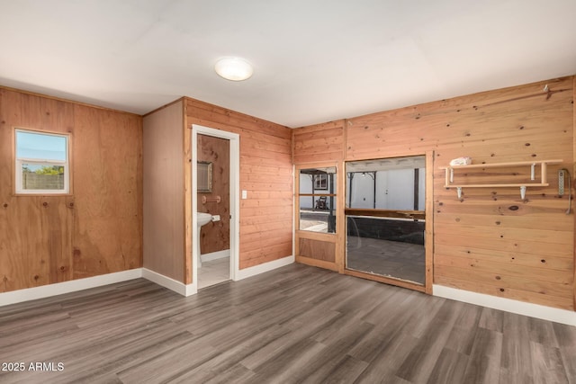 unfurnished living room featuring wooden walls, baseboards, and wood finished floors