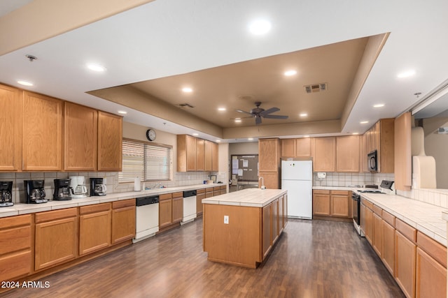 kitchen featuring a center island, a raised ceiling, white appliances, and dark wood-type flooring