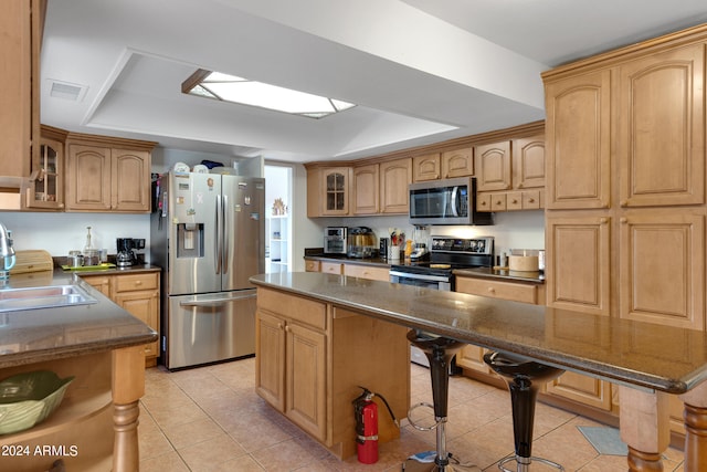 kitchen featuring a raised ceiling, sink, a kitchen island, stainless steel appliances, and a breakfast bar