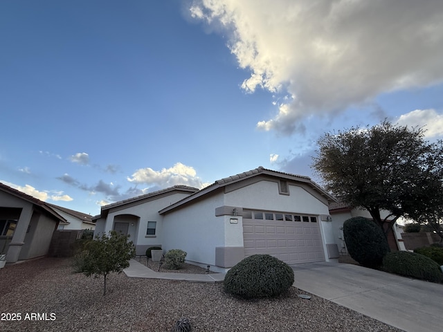 ranch-style house featuring driveway, an attached garage, a tiled roof, and stucco siding