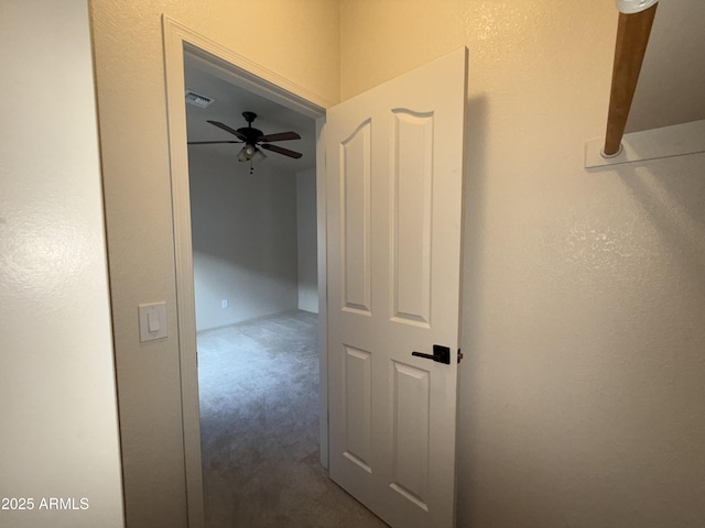 hallway with a textured wall, carpet flooring, and visible vents