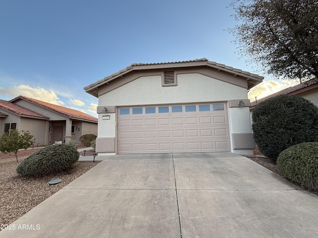 ranch-style house featuring a garage, a tiled roof, concrete driveway, and stucco siding