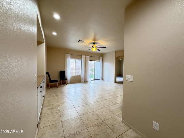 spare room with ceiling fan, light tile patterned floors, arched walkways, visible vents, and baseboards