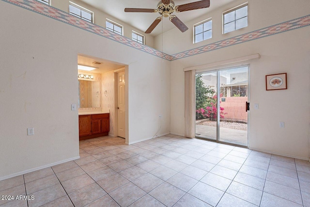 tiled empty room with ceiling fan and a towering ceiling