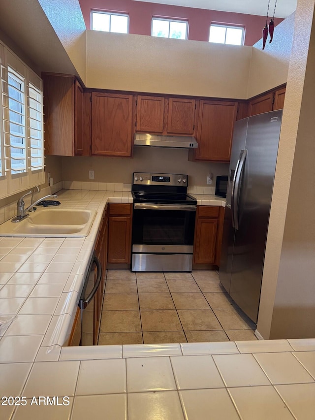 kitchen featuring sink, tile counters, pendant lighting, light tile patterned floors, and appliances with stainless steel finishes