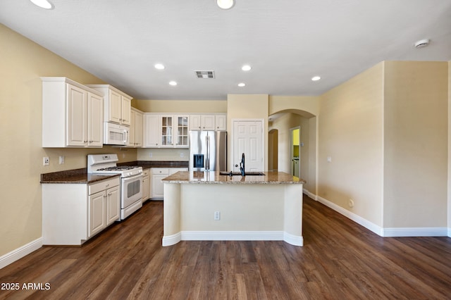 21017 W Edith Way, Buckeye, AZ 85396 - kitchen with white appliances, arched walkways, a center island with sink, dark wood finished floors, and glass insert cabinets
