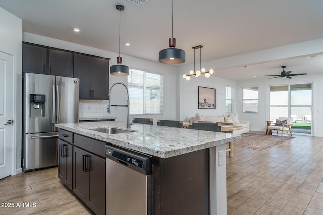 kitchen featuring stainless steel appliances, a sink, open floor plan, wood tiled floor, and tasteful backsplash