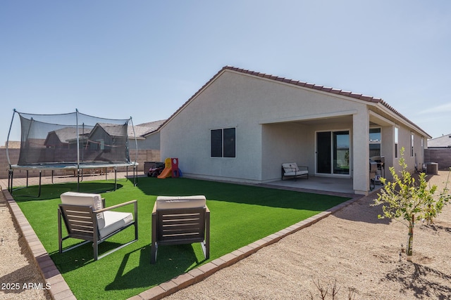 back of property featuring a trampoline, a patio, stucco siding, a lawn, and fence