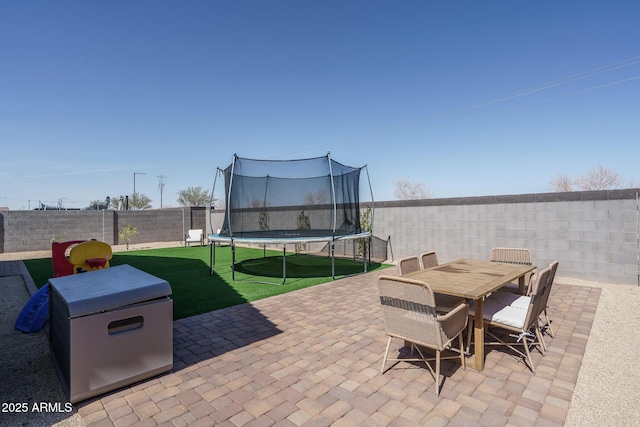 view of patio / terrace with outdoor dining area, a trampoline, and a fenced backyard