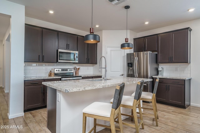 kitchen featuring stainless steel appliances, a sink, light wood-style flooring, and dark brown cabinetry