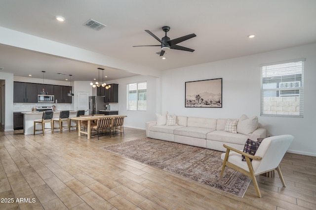 living area with light wood finished floors, visible vents, and ceiling fan with notable chandelier