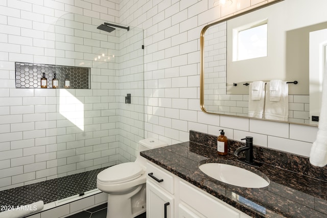 bathroom with tile walls, tiled shower, backsplash, vanity, and toilet