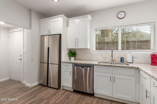 kitchen with stainless steel appliances, a sink, white cabinetry, light wood finished floors, and tasteful backsplash