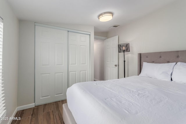 bedroom with dark wood-style flooring, a closet, visible vents, and baseboards