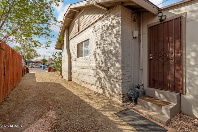 doorway to property with driveway, brick siding, and fence