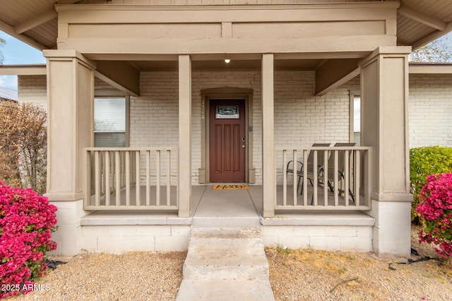 view of exterior entry featuring covered porch and brick siding