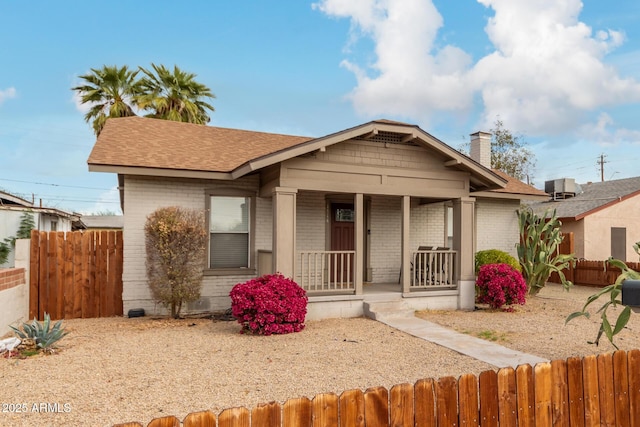 bungalow-style house featuring covered porch, brick siding, a chimney, and a fenced front yard