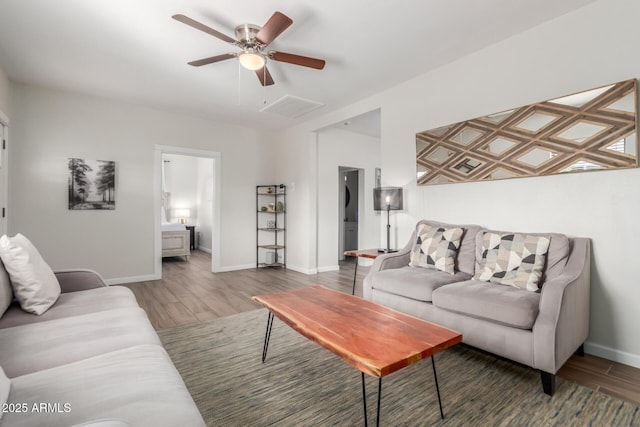 living room with a ceiling fan, visible vents, baseboards, and wood finished floors