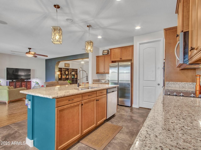 kitchen featuring sink, light stone counters, appliances with stainless steel finishes, an island with sink, and pendant lighting